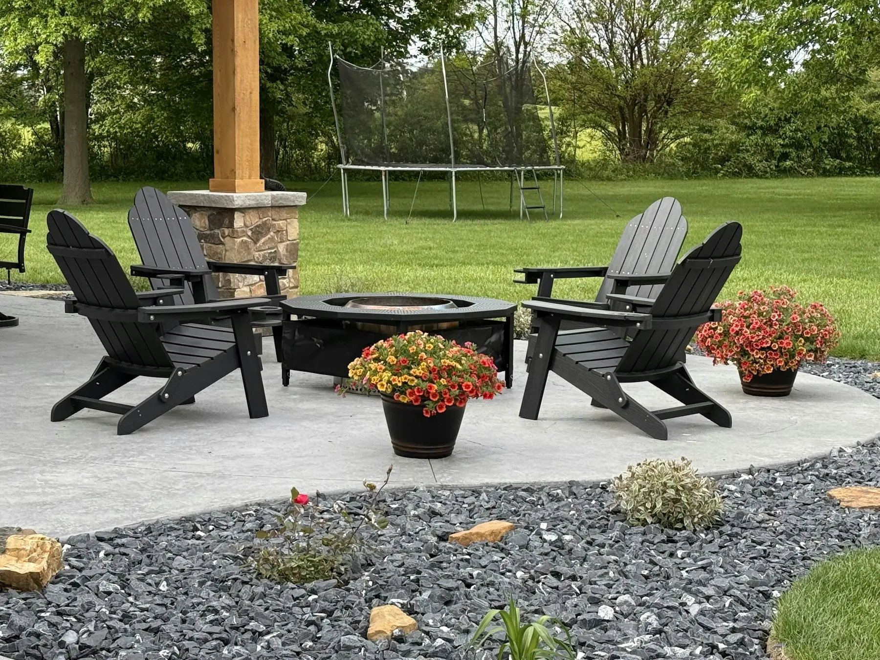 Backyard fire pit patio with adirondack chairs and flower beds