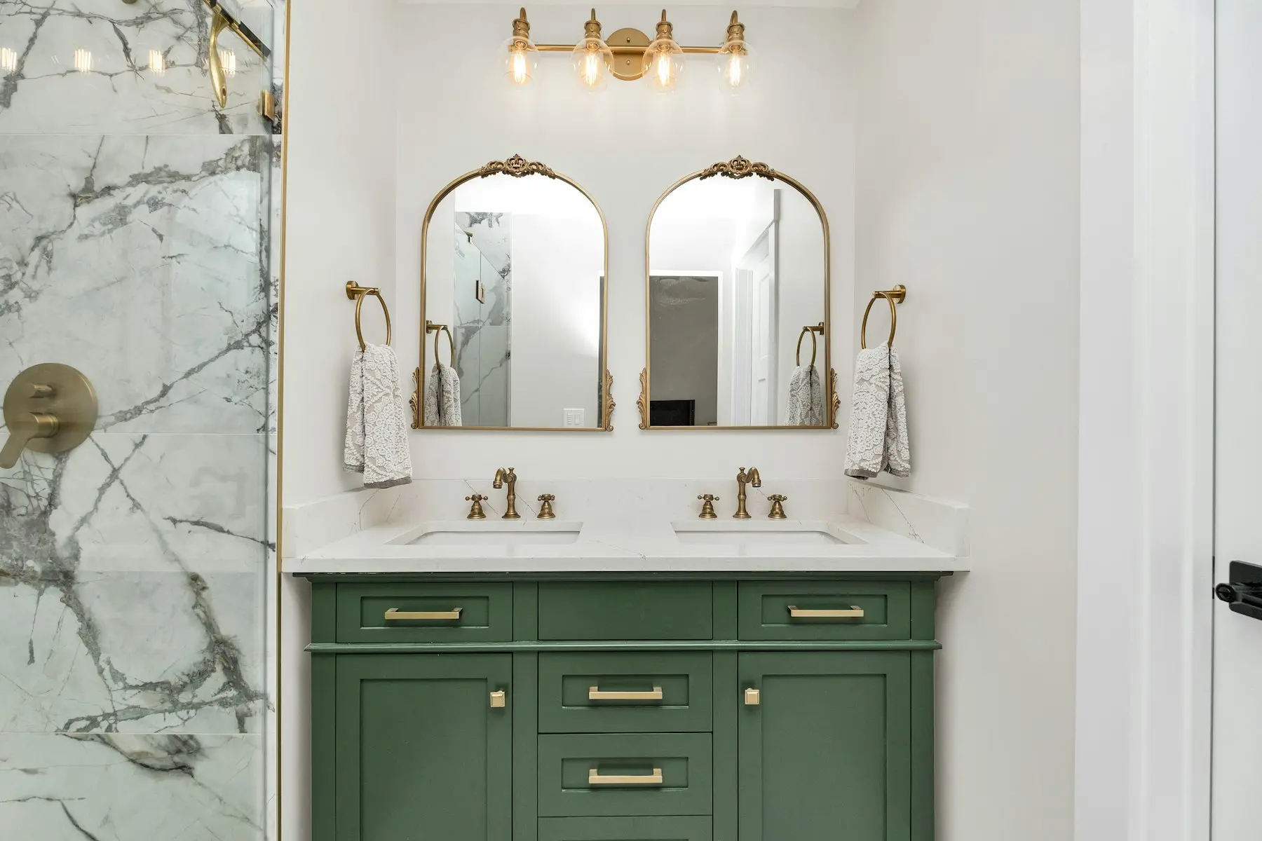 Green double vanity with brass mirrors and marble-look tile