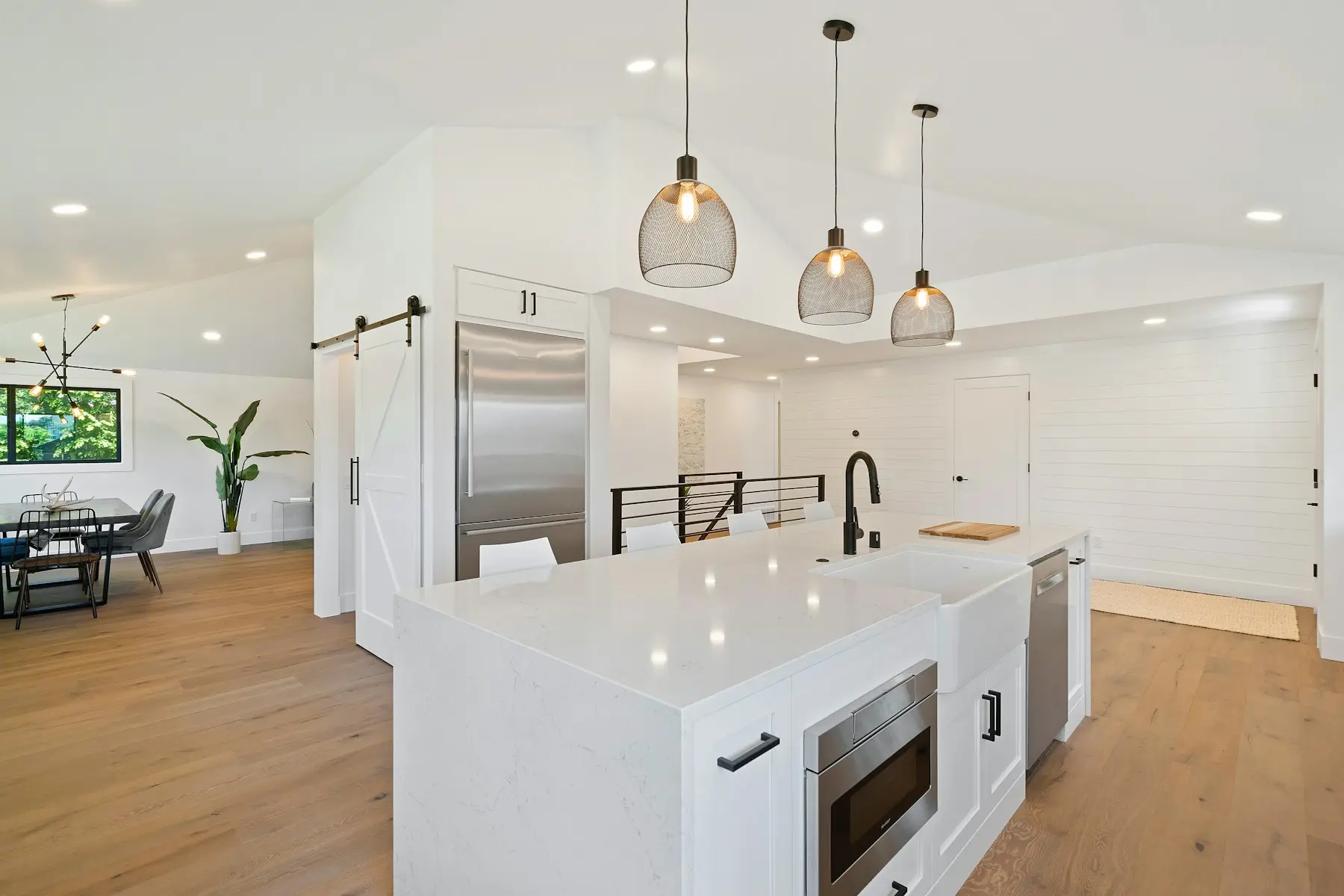 Open-concept white kitchen with waterfall island and glass pendants
